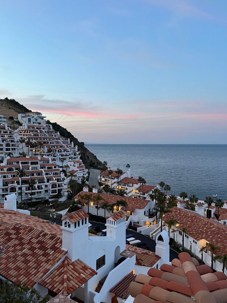 an aerial view of houses and the ocean at dusk, with mountains in the background