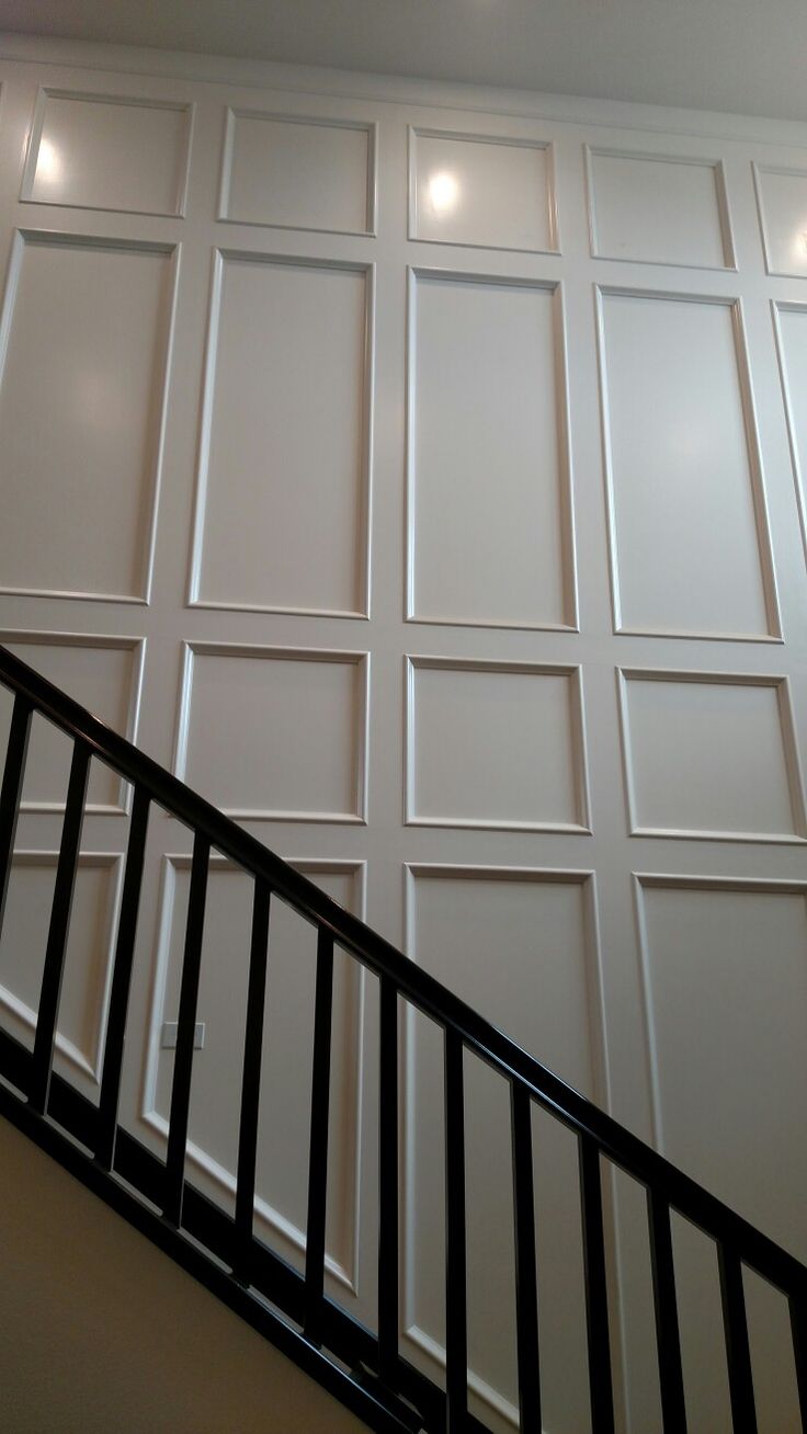 a stair case with white paneling and black handrails in front of a wall