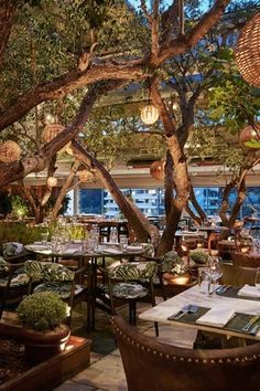 an outdoor dining area with tables, chairs and lamps hanging from the tree's branches