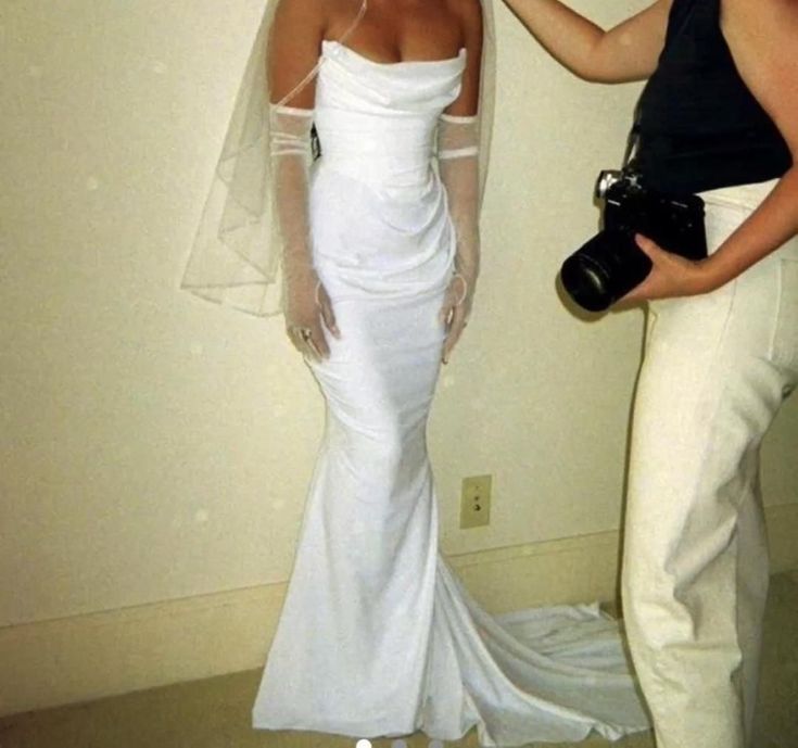 a woman in a white wedding dress is taking a photo with her camera and another person standing next to her