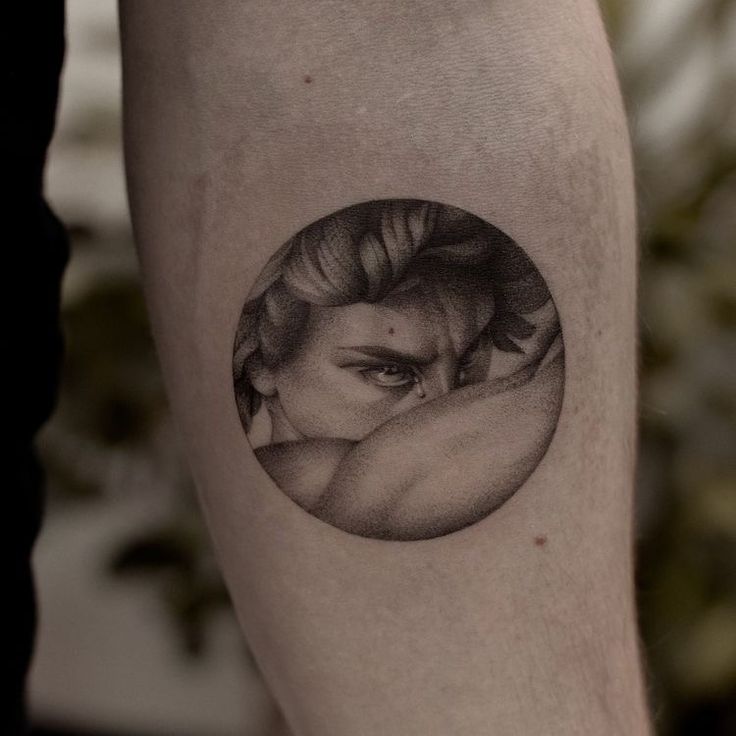 a black and white photo of a woman's face in a circle tattoo on the leg