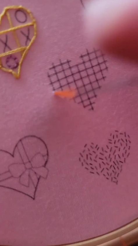 someone is stitching hearts on a pink piece of fabric with yellow thread and scissors