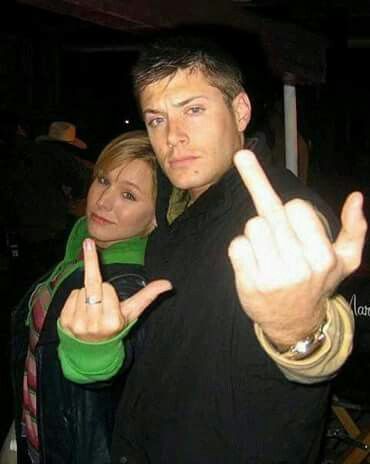 a man and woman standing next to each other giving the peace sign