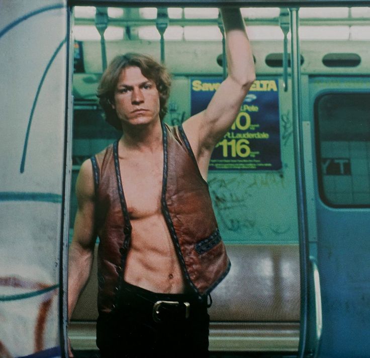 a man with no shirt on standing in front of a subway car holding his arm up