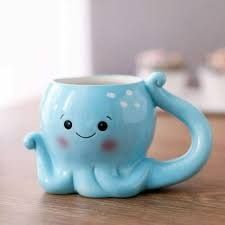 a blue coffee cup with a smiling octopus on it's side sitting on a table