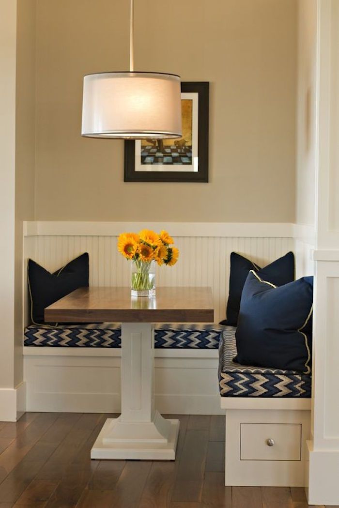 a dining room table with two benches and flowers in a vase on the bench next to it