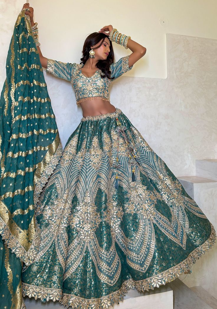 a woman in a green and gold lehenga with her hands on her head