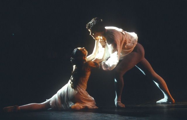 two dancers performing on stage in the dark