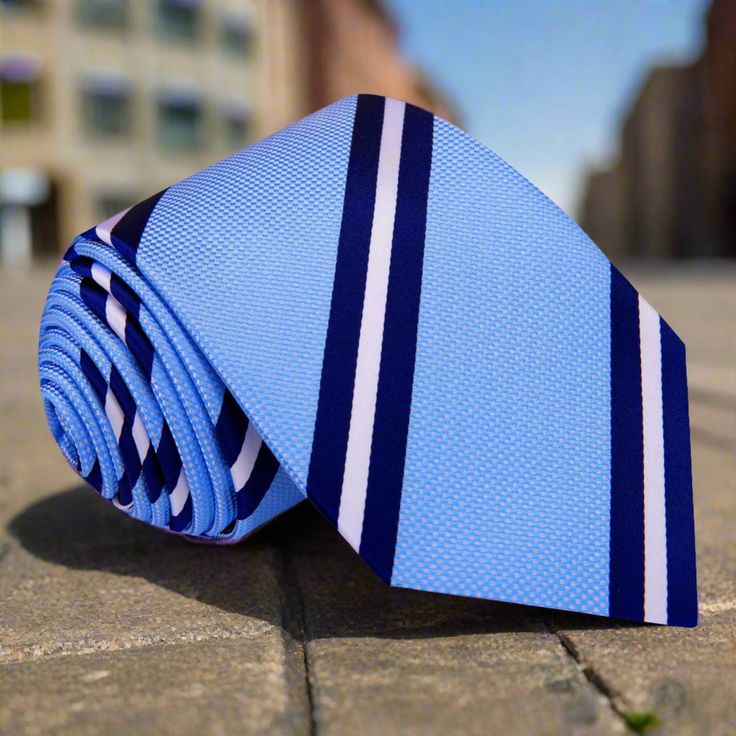 This light blue silk necktie with dark blue and white stripes is a refined addition to any gentleman's wardrobe. The smooth texture and sophisticated pattern offer a stylish touch that is versatile for various dress codes. Recommended Dress Shirts: White Dress Shirt: Provides a classic, crisp look that highlights the tie's colors. Light Blue Dress Shirt: Creates a harmonious, monochromatic ensemble. Dark Blue Dress Shirt: Offers a bold contrast that complements the tie's stripes. Light Grey Dres Elegant Blue Tie For Business, Classic Blue Ties For Business, Classic Blue Business Ties, Elegant Blue Neckwear For Business, Classic Blue Neckwear For Business, Elegant Light Blue Tie For Black Tie Events, Classic Blue Business Neckwear, Classic Blue Ties For Formal Occasions, Elegant Blue Suit And Tie Accessories For Office