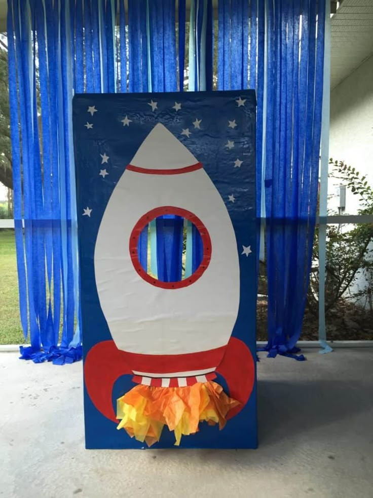 a cardboard rocket ship sitting on top of a cement floor in front of blue curtains