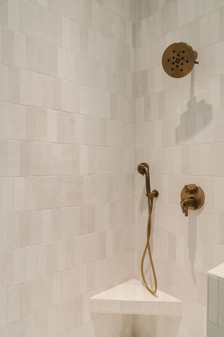 a shower head and hand held shower faucet in a white tiled bathroom area