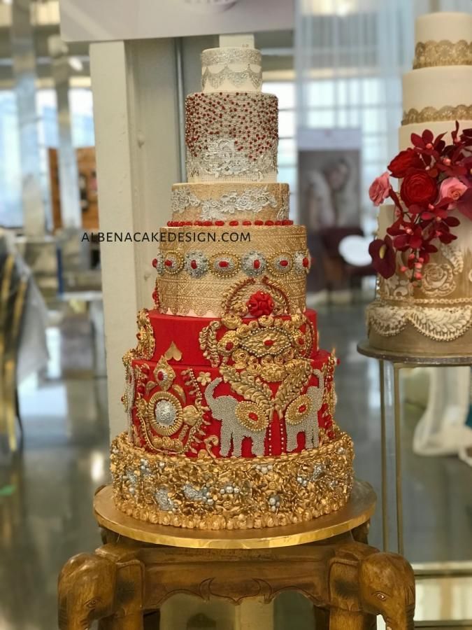 three tiered wedding cake with red and gold decorations on display in front of glass windows