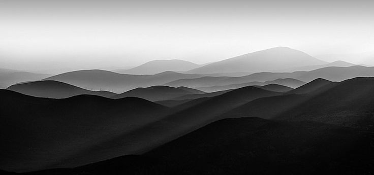 black and white photograph of mountains in the distance with fog coming from them, taken on an overcast day