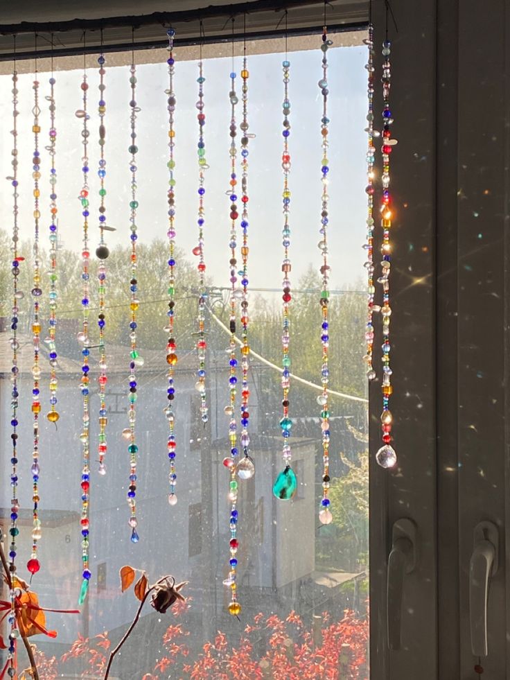 a window with beads hanging from it's side and flowers in the foreground