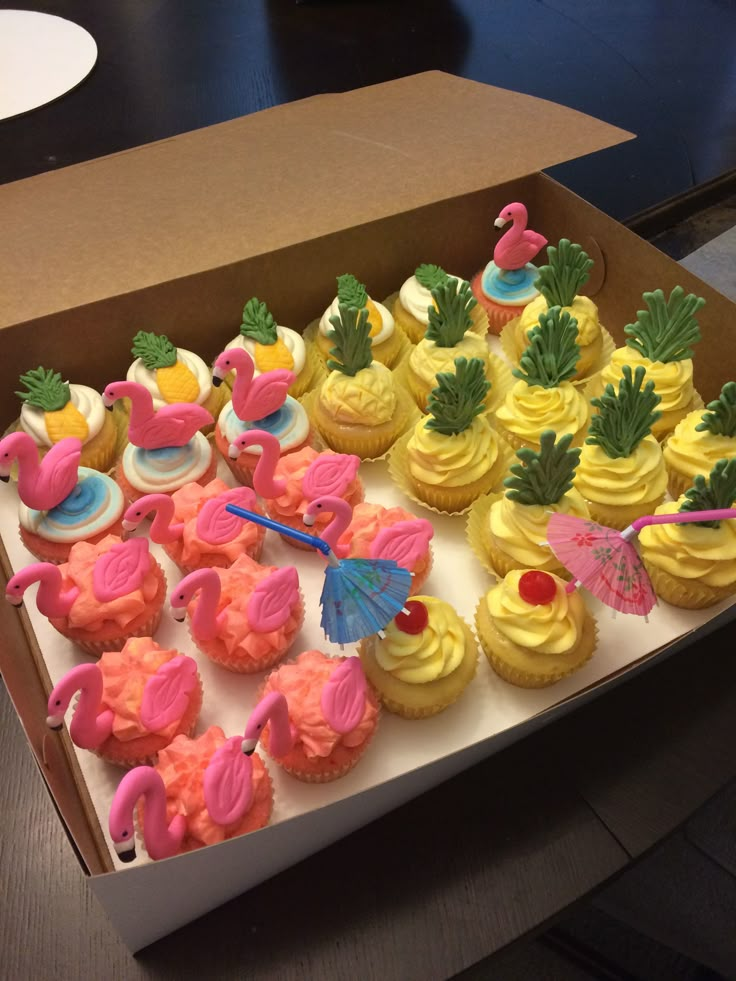 a box filled with lots of cupcakes covered in frosting and pineapple decorations