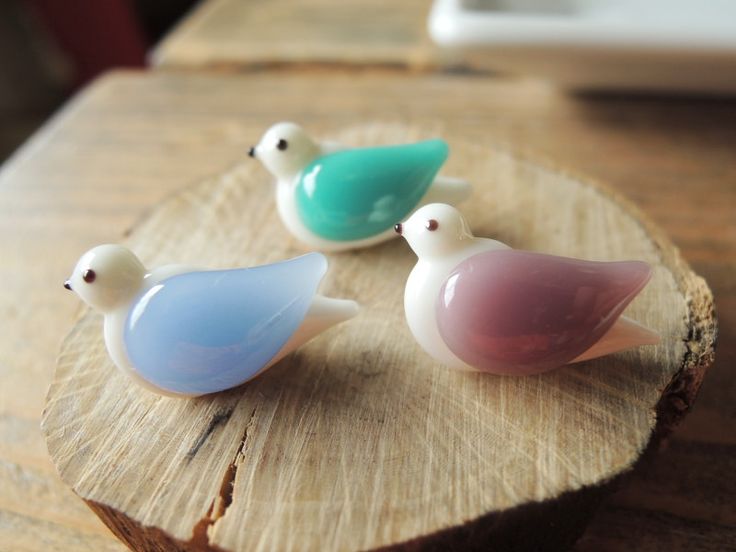 three small glass birds sitting on top of a piece of wood next to each other