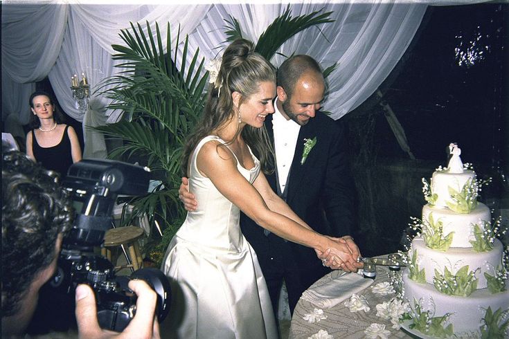 a bride and groom cutting their wedding cake at an outdoor reception in front of photographers