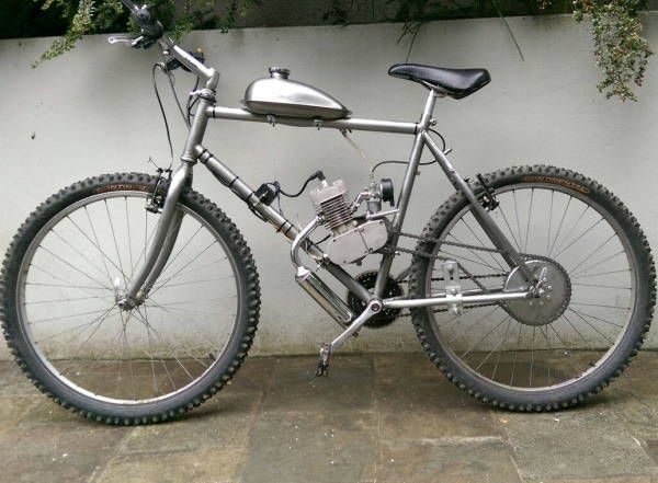 a silver bike parked next to a white wall and green plants on the side of it