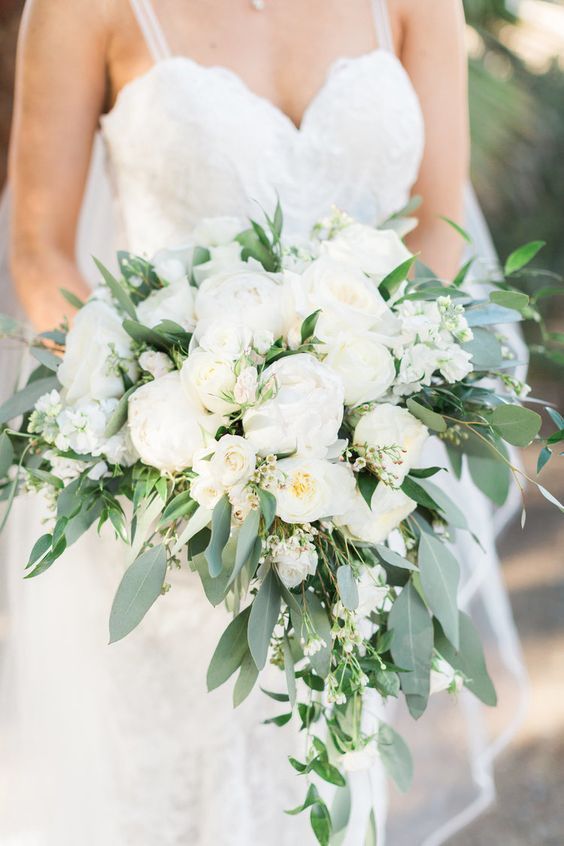 a bridal holding a bouquet of white flowers and greenery in her left hand