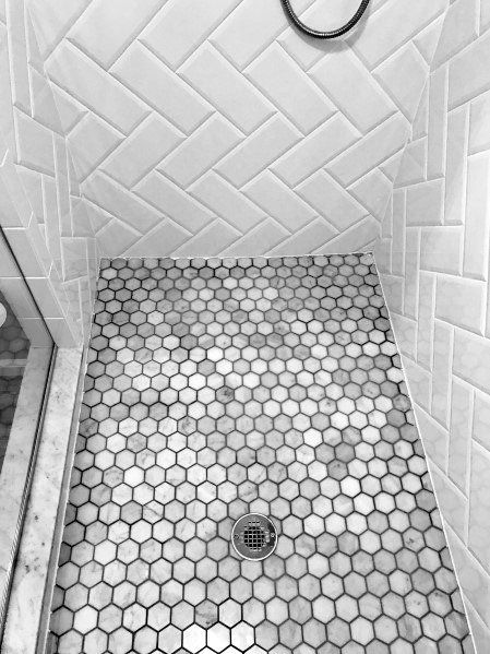 a bathroom shower with hexagonal tiles and a standup shower head in the corner