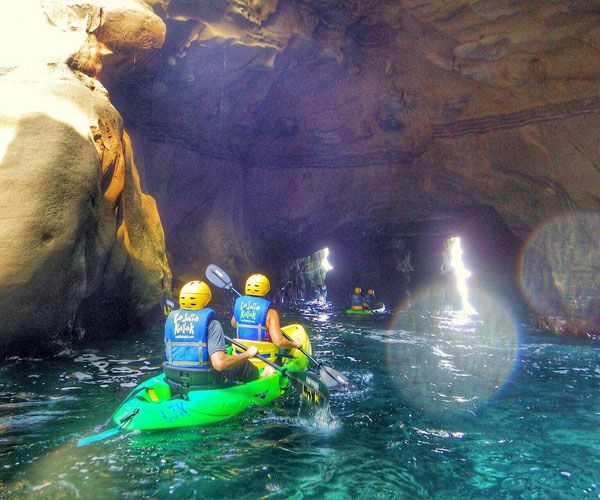 two people in green kayaks paddling through an underground cave with blue water and large rocks