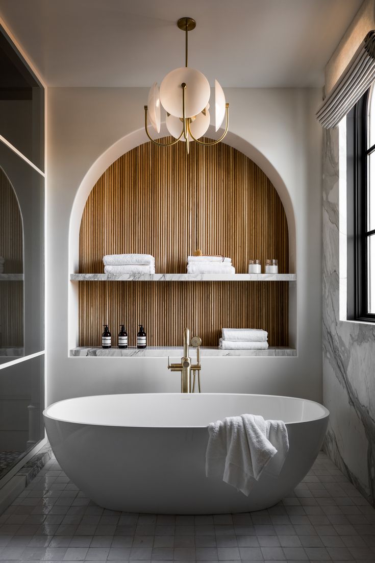 a large white bath tub sitting under a window next to a shelf filled with towels