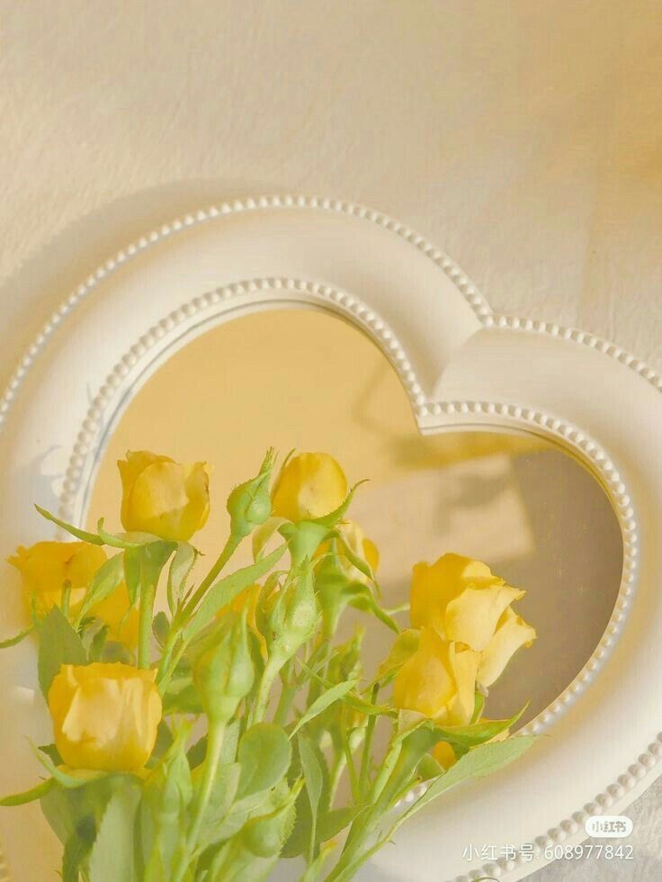 some yellow flowers are in a white heart shaped vase on a table with a mirror