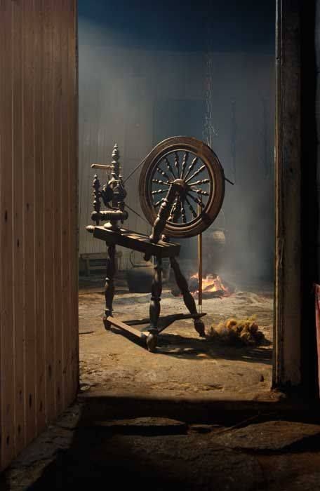 a black and white photo of a spinning wheel in a room with light coming through the door