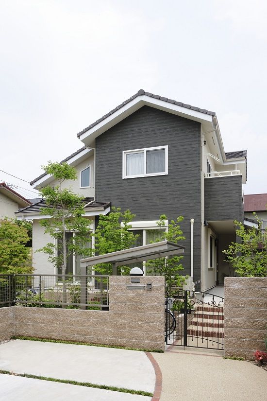 a black house with a white fence and trees in the front yard, along with a bicycle parked on the driveway