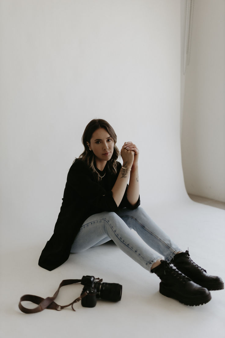 a woman sitting on the floor with her legs crossed, holding a camera and taking a photo