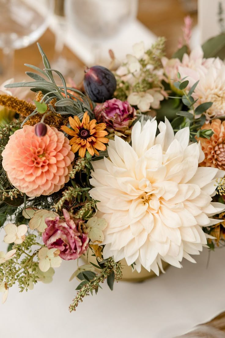 an arrangement of flowers on a table with wine glasses and napkins in the background