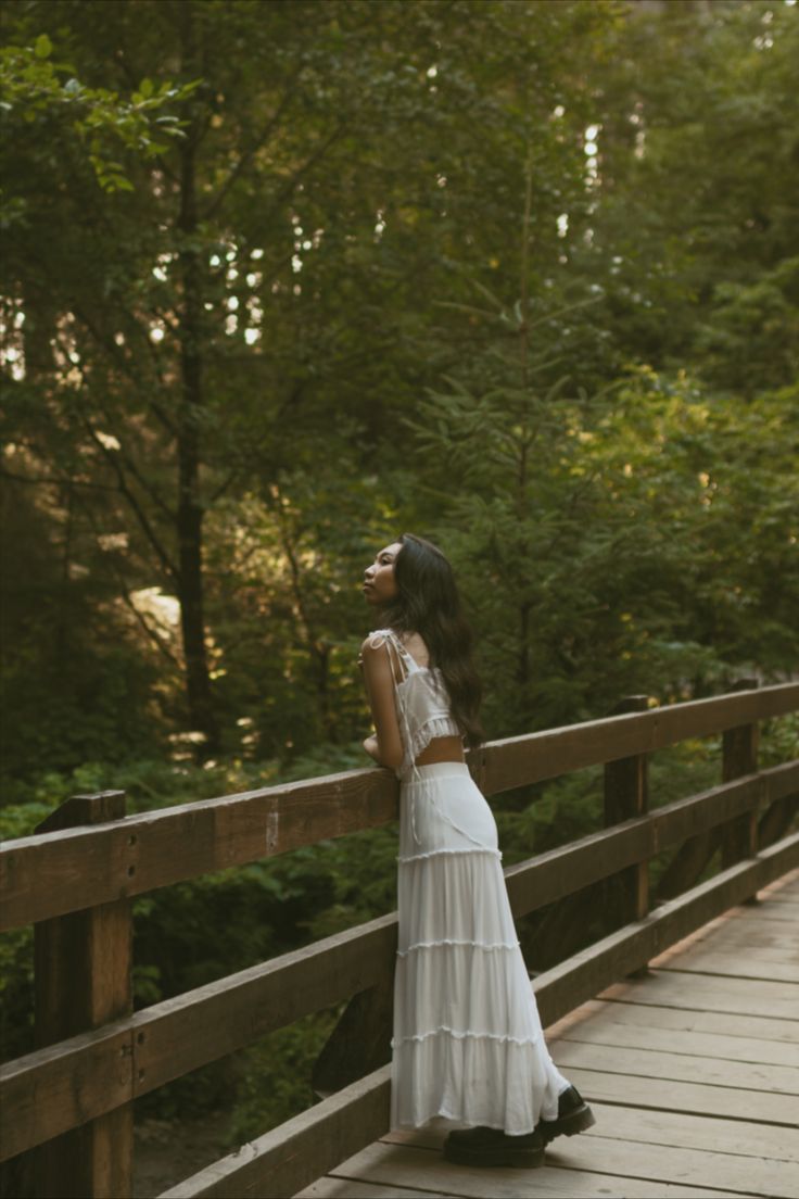 a woman is standing on a bridge in the woods looking up at something she's holding