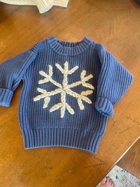 a blue sweater with white snowflakes on it sitting on a wooden floor next to a person's feet