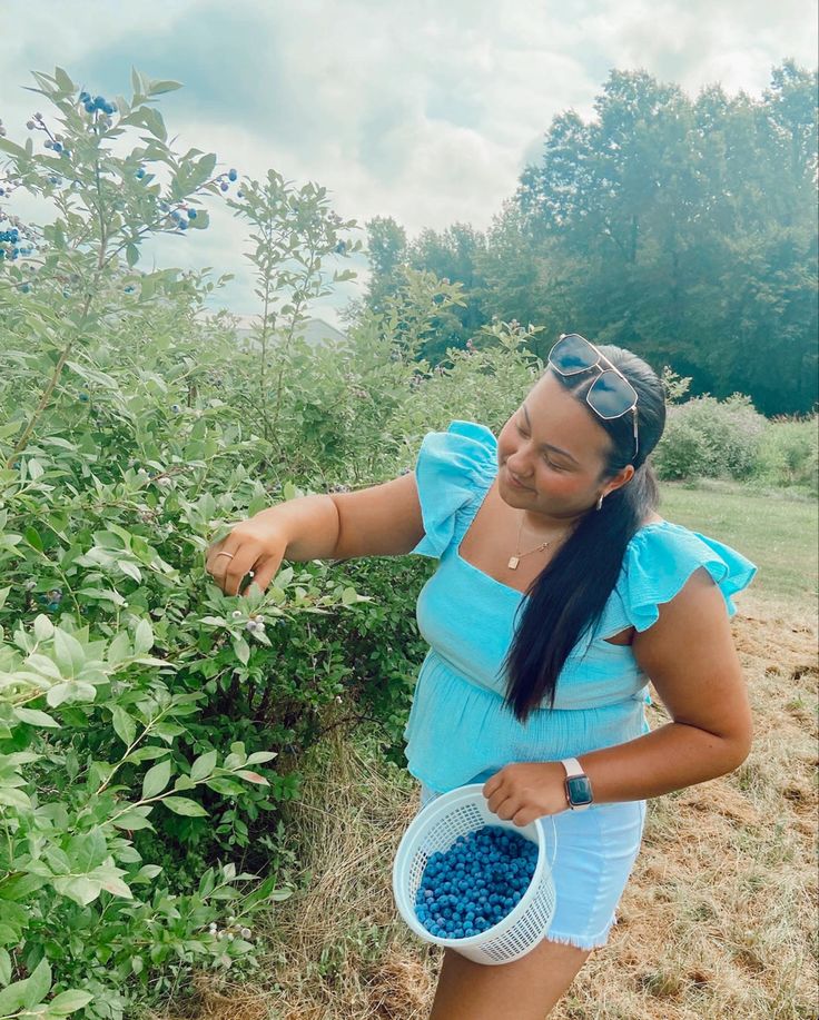 a woman picking blueberries from a bush