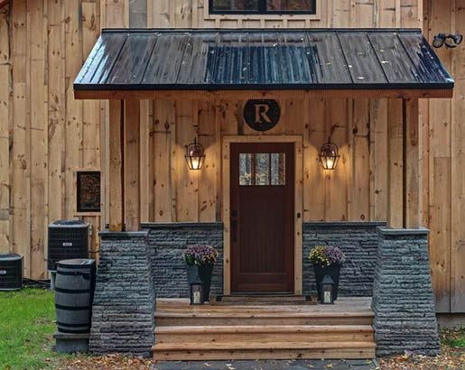 a wooden building with a metal roof and two large barrels in front of the door