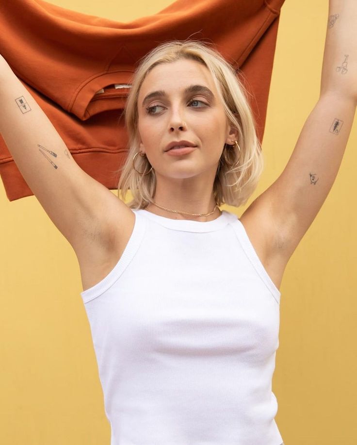 a woman in white shirt holding up an orange scarf over her head with both hands