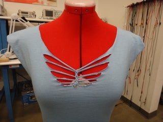 a mannequin with red and blue wings on it's back, sitting in front of a sewing machine