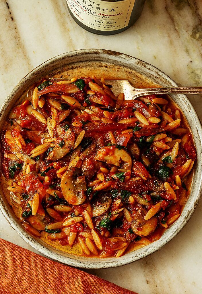 a bowl filled with pasta and sauce on top of a table next to a bottle of wine