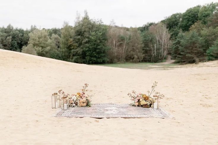 two vases with flowers sit on a blanket in the middle of a sandy area