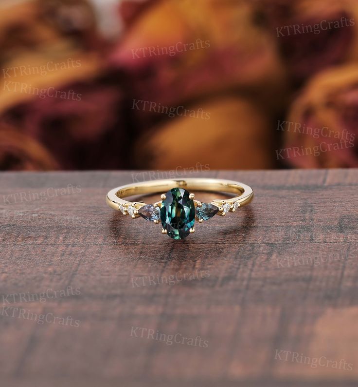 a gold ring with blue and green stones on it sitting on a wooden table in front of a couch