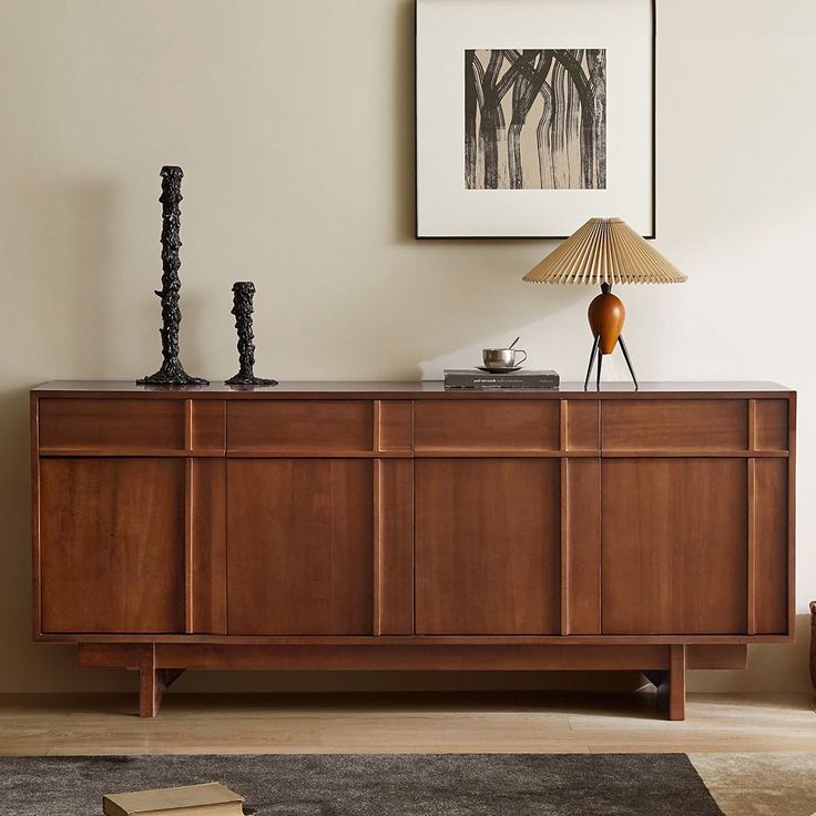 a sideboard with two lamps on top of it in front of a framed painting