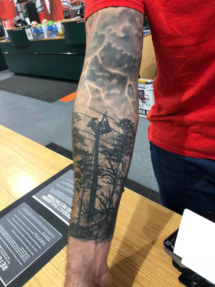 a man's arm with a tree and clouds tattoo on the left side of his arm