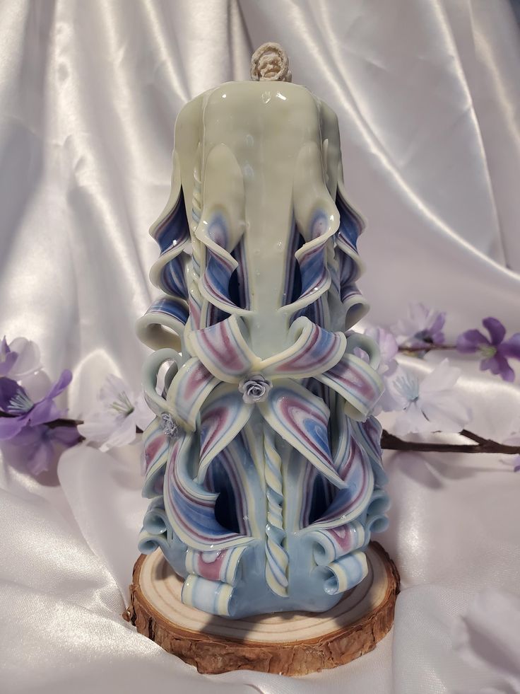 a decorative candle is sitting on top of a piece of wood with purple flowers around it