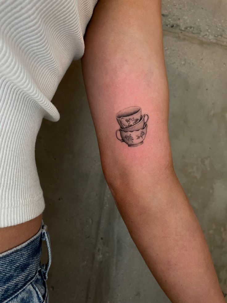 a woman's arm with a small cup tattoo on it