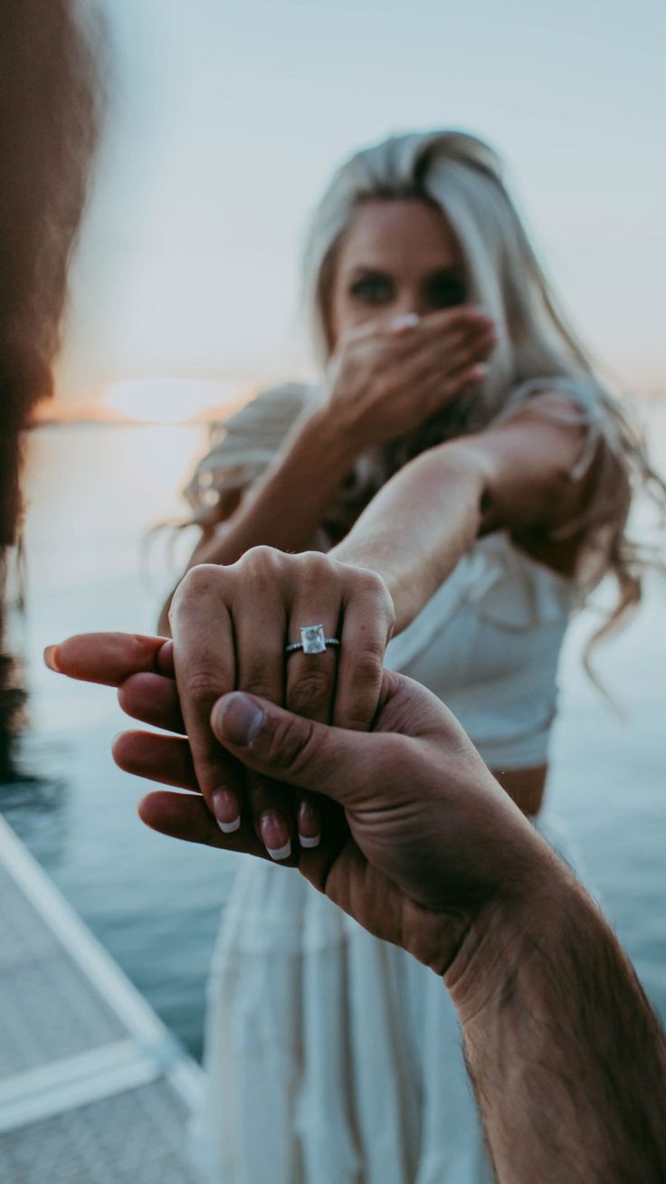 a man and woman holding each other's hand near the water with their fingers together