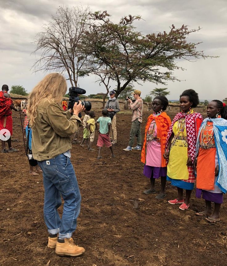 a group of people standing on top of a dirt field next to each other in front of a tree