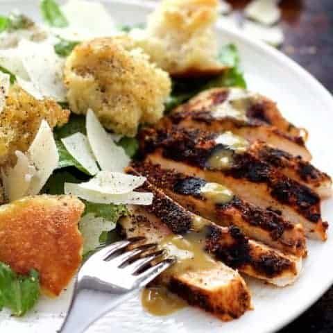 a white plate topped with meat and salad next to a fork on top of a table