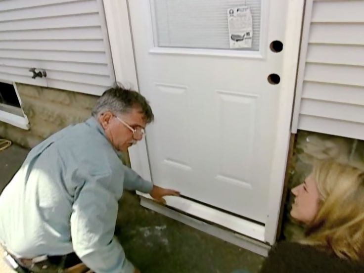 a man and woman standing in front of a white door next to each other on the side of a house