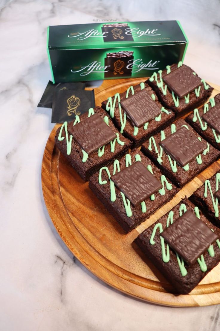 a wooden plate topped with chocolate brownies covered in green icing next to a box of mints