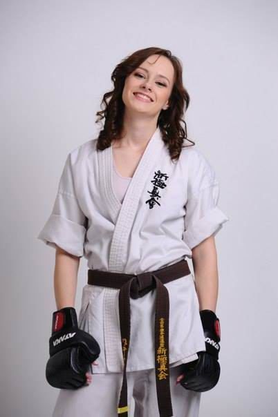 a woman in a white kimono and black gloves smiles at the camera while standing with her hands on her hips